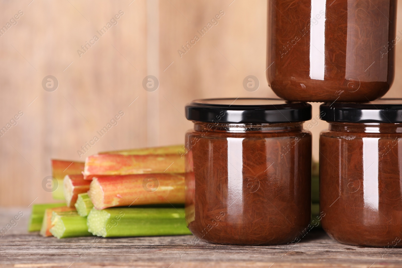 Photo of Jars of tasty rhubarb jam and stalks on wooden table, closeup