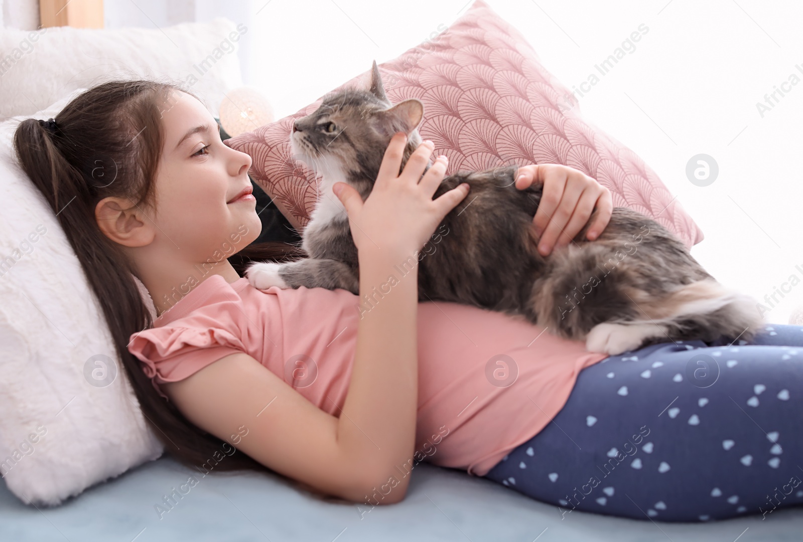 Photo of Cute little girl with cat lying on bed at home