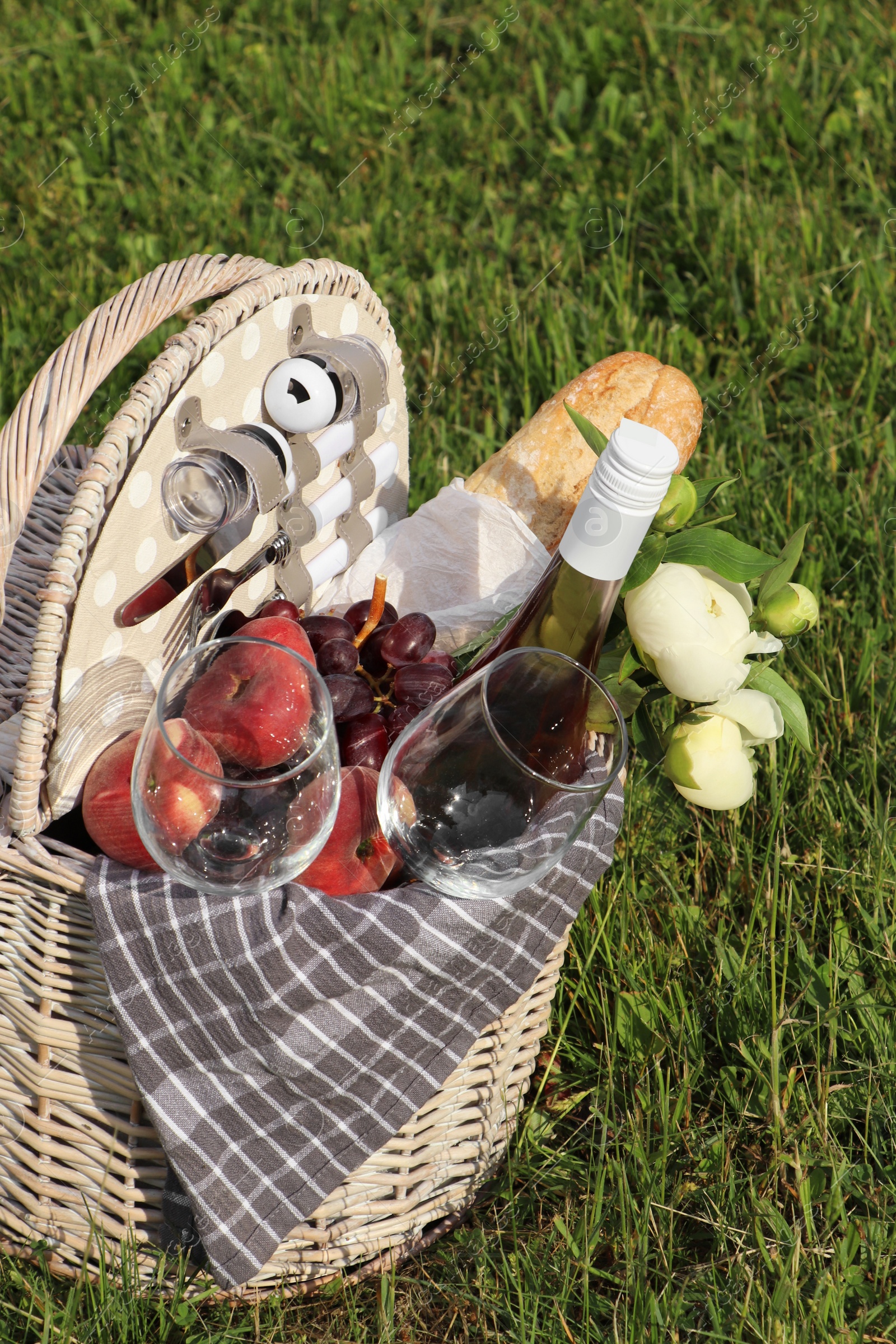 Photo of Picnic basket with tasty food, flowers and cider on grass