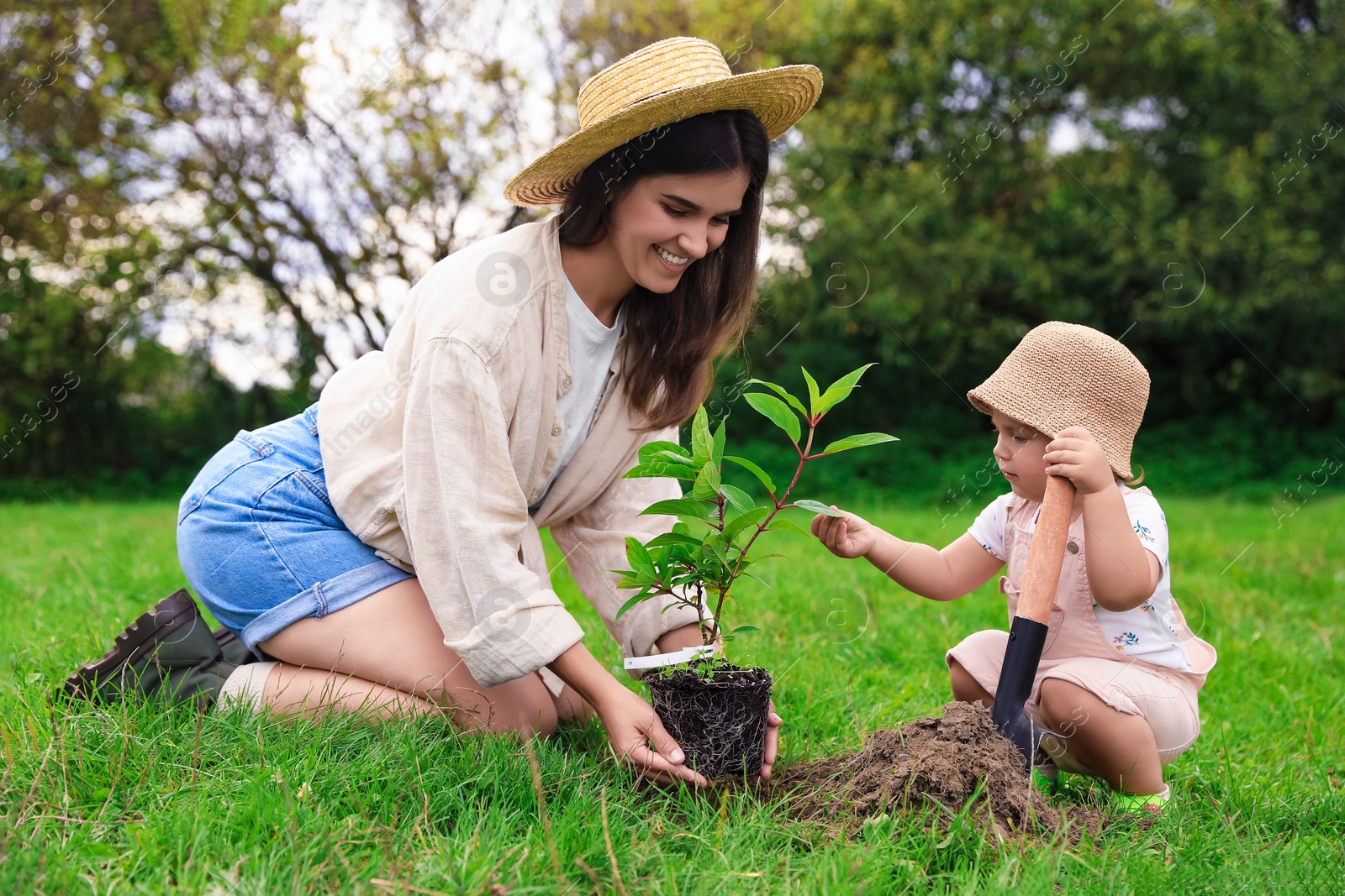 Photo of Mother and her baby daughter planting tree together in garden