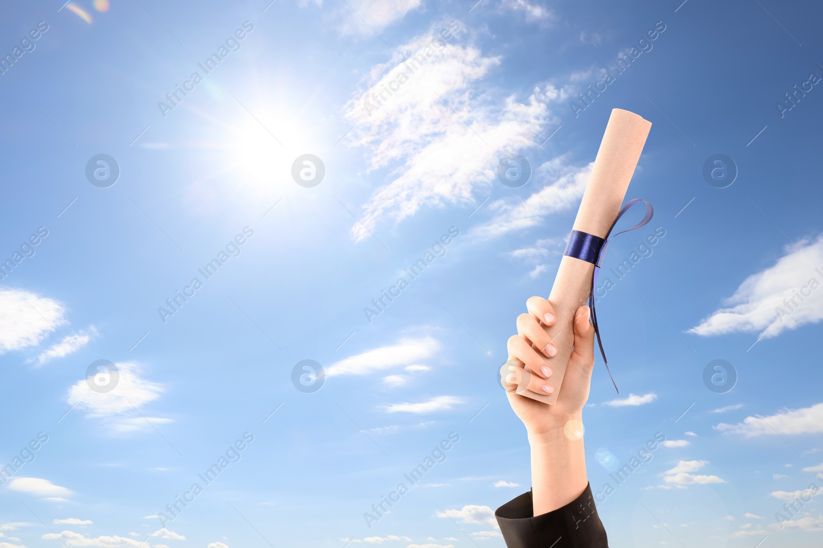 Image of Graduated student holding diploma against blue sky on sunny day, closeup