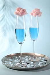 Photo of Cotton candy cocktails in glasses and confetti on light blue background