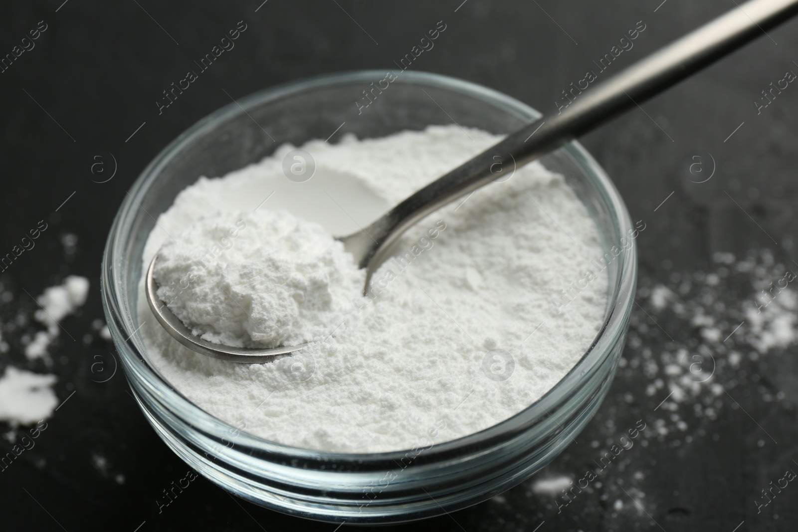 Photo of Baking powder in bowl and spoon on black table, closeup