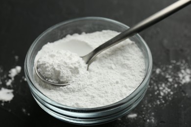 Baking powder in bowl and spoon on black table, closeup