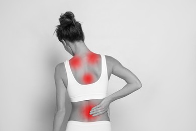 Woman suffering from back pain on light background