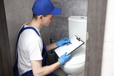 Young plumber writing results of examining toilet bowl in water closet