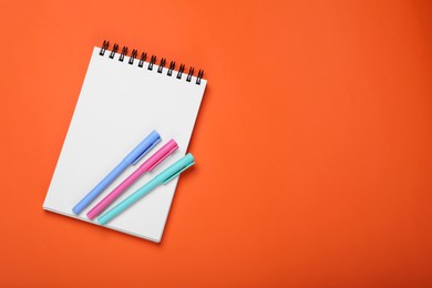 Photo of Blank office notebook and pens on orange background, top view. Space for text