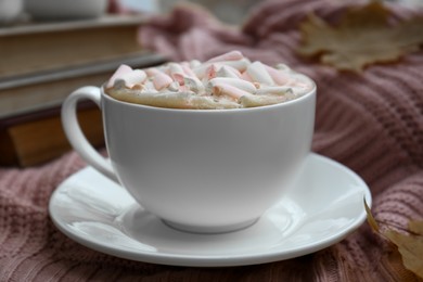 Photo of Cup of tasty hot drink with marshmallows on blanket, closeup. Autumn coziness