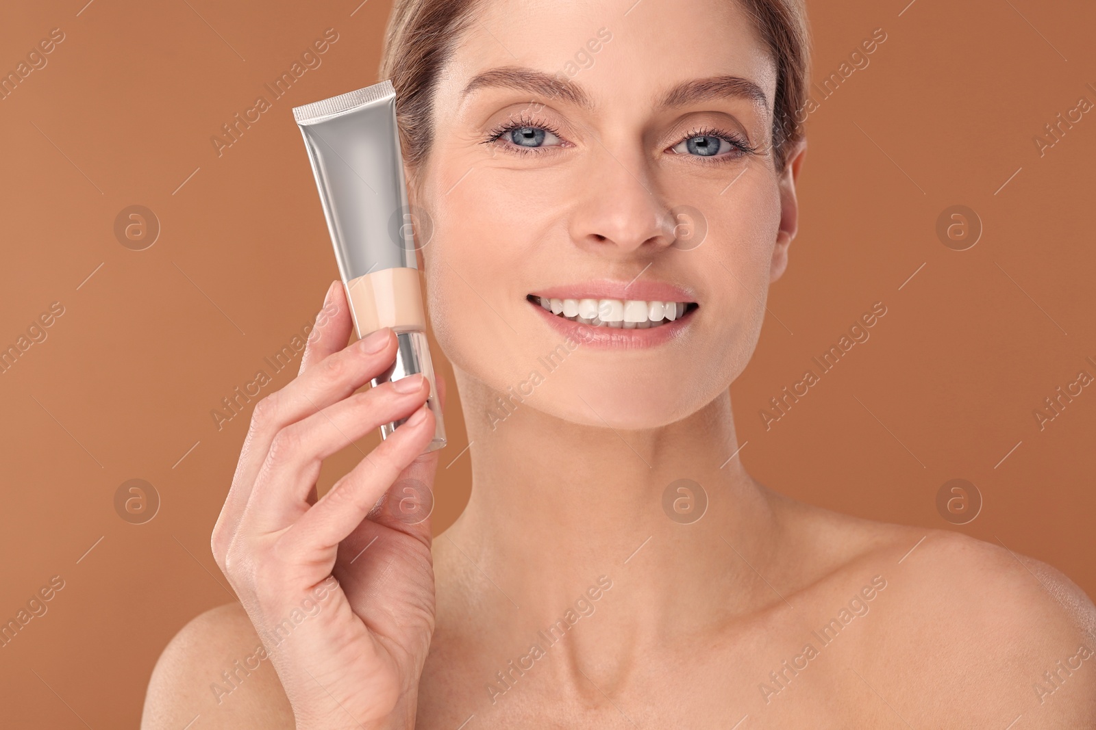 Photo of Woman holding tube of foundation on brown background