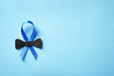 Photo of Blue ribbon with small bow tie on color background, top view. Cancer awareness