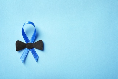 Blue ribbon with small bow tie on color background, top view. Cancer awareness