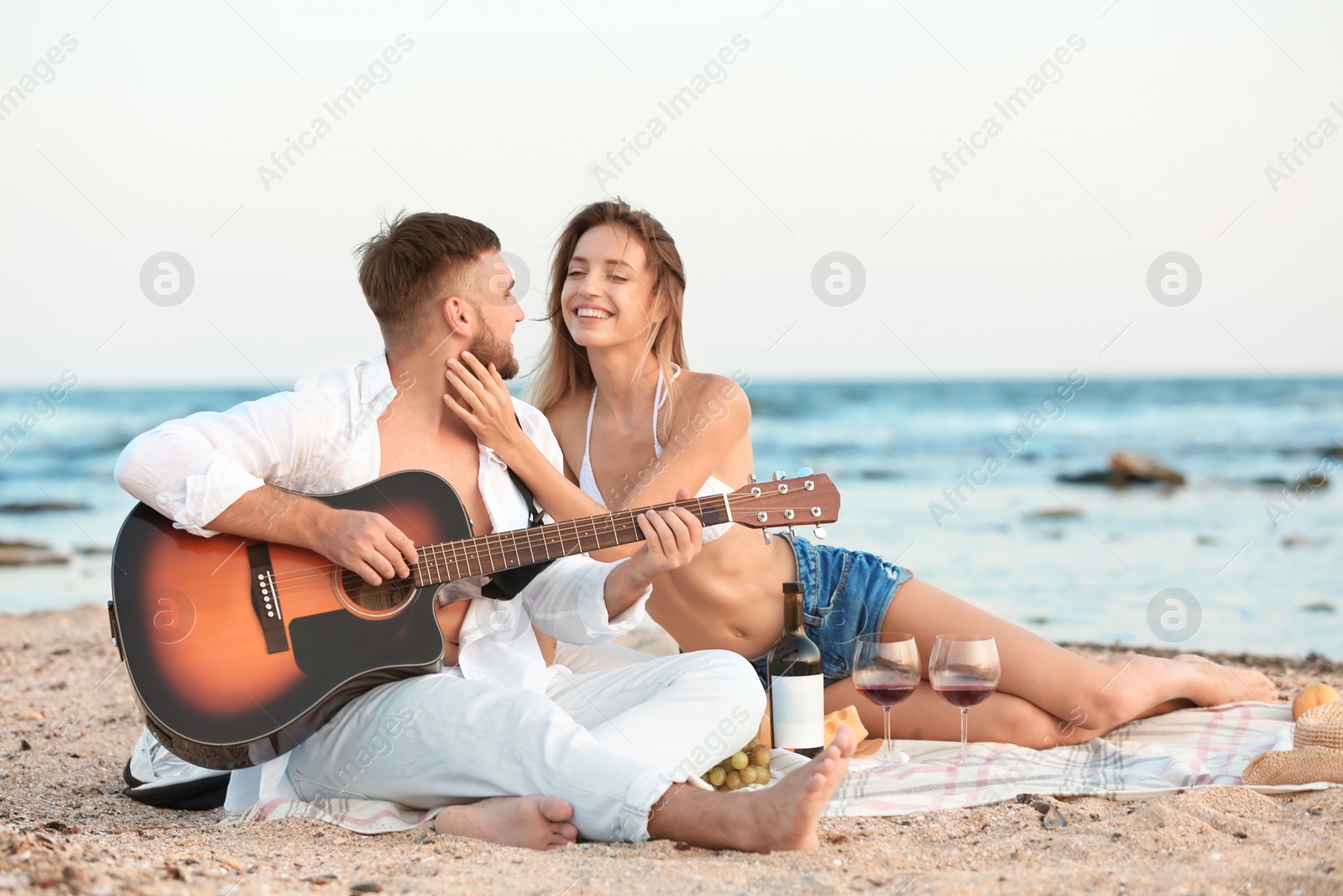Photo of Young couple with guitar having romantic dinner on beach