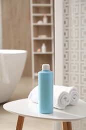 Bottle of shower gel and fresh towels on white table in bathroom