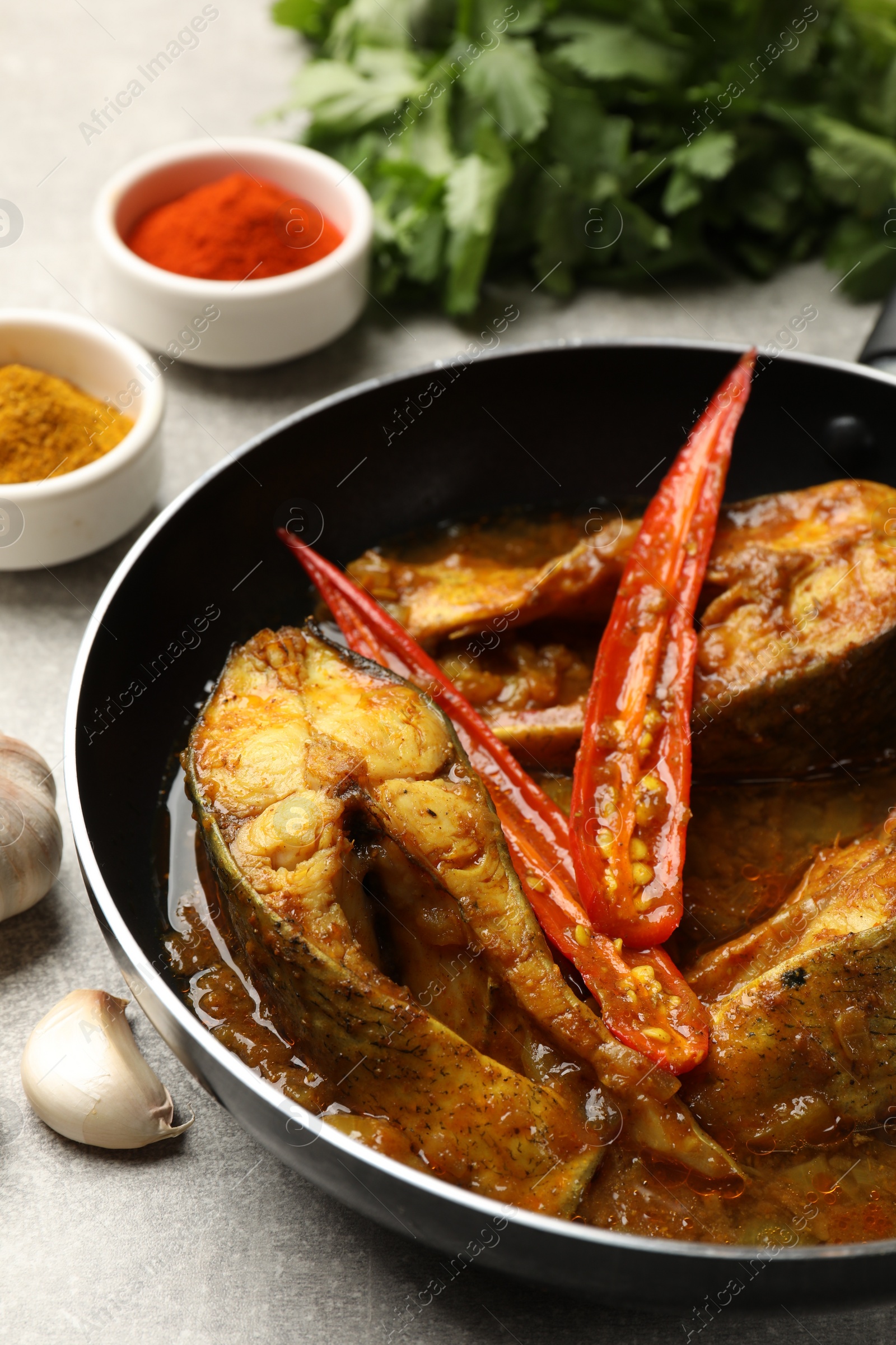 Photo of Tasty fish curry in frying pan and ingredients on light grey table, closeup. Indian cuisine