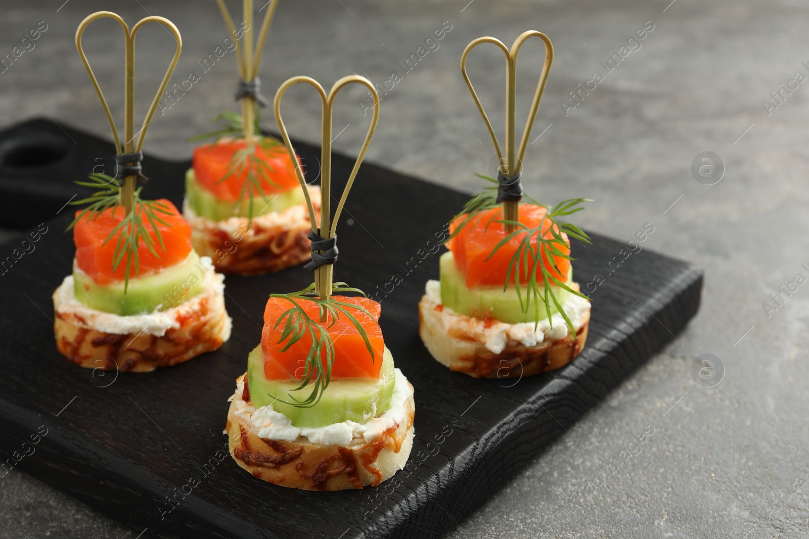 Photo of Tasty canapes with salmon, cucumber, bread and cream cheese on grey table, closeup