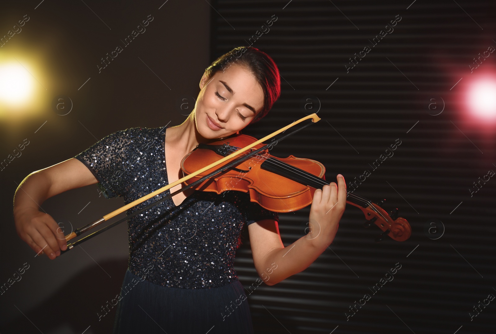 Photo of Beautiful young woman playing violin in dark room