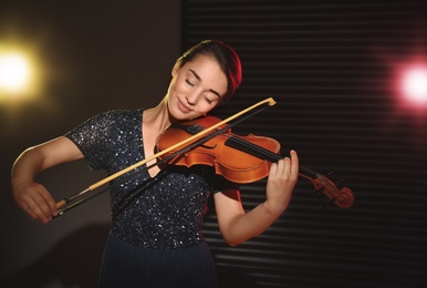 Beautiful young woman playing violin in dark room