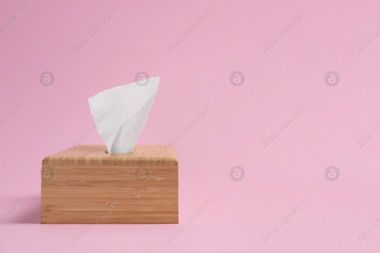 Photo of Wooden holder with paper tissues on pink background. Space for text