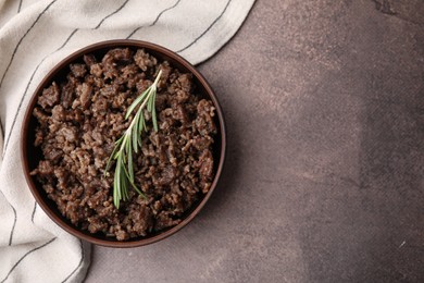 Photo of Fried ground meat in bowl and rosemary on brown textured table, top view. Space for text