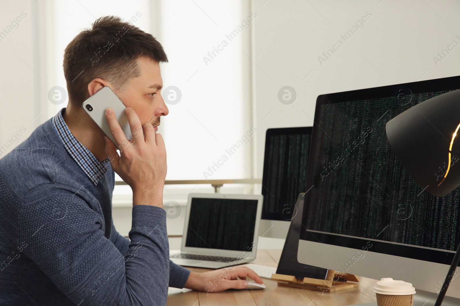 Photo of Programmer talking on phone while working at desk in office