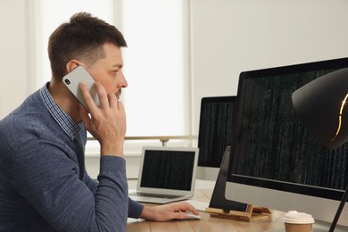 Programmer talking on phone while working at desk in office