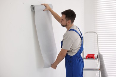 Photo of Man hanging stylish gray wallpaper in room