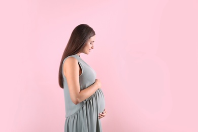 Photo of Beautiful pregnant woman holding hands on belly against color background. Space for text