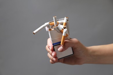 Photo of Stop smoking. Woman holding pack with broken cigarettes on grey background, closeup