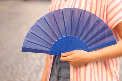 Photo of Woman with blue hand fan outdoors, closeup