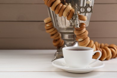 Photo of Cup of tea and delicious ring shaped Sushki (dry bagels) on white wooden table, space for text