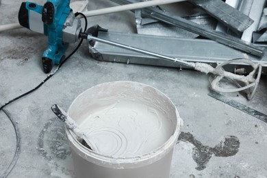 Photo of Bucket with plaster and putty knife near construction equipment on concrete floor