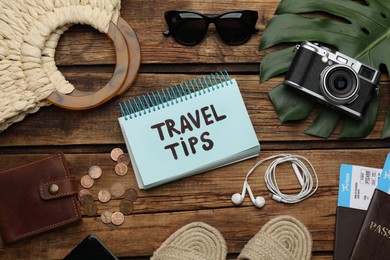 Photo of Notebook with phrase Travel Tips and tourist items on wooden table, flat lay