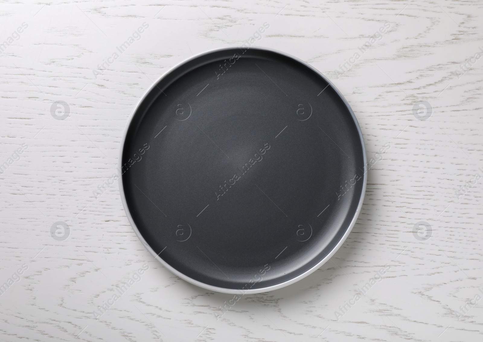 Photo of New dark plate on white wooden table, top view