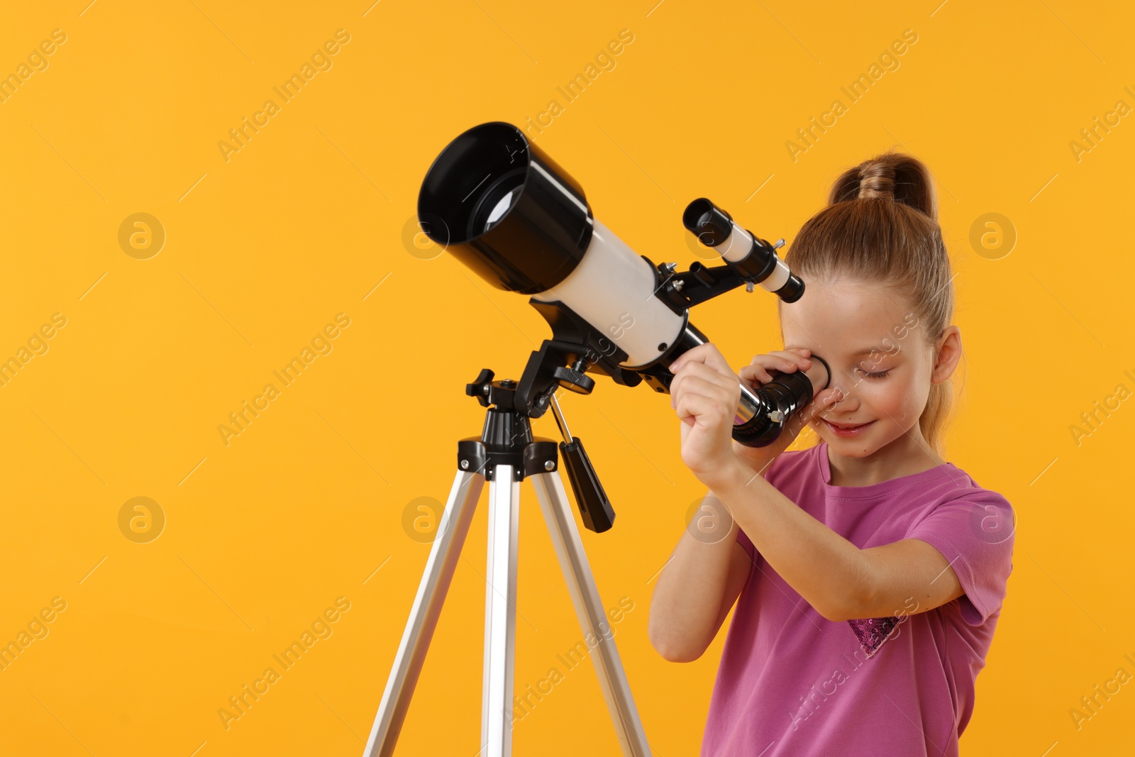 Photo of Happy little girl looking at stars through telescope on orange background, space for text