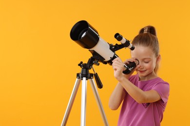 Photo of Happy little girl looking at stars through telescope on orange background, space for text