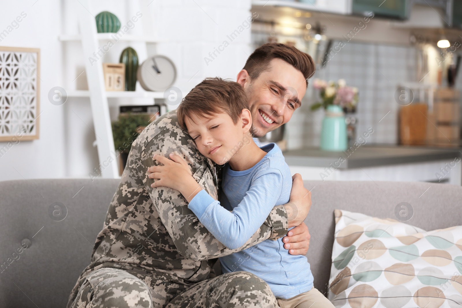 Photo of Young man in military uniform with his little son at home