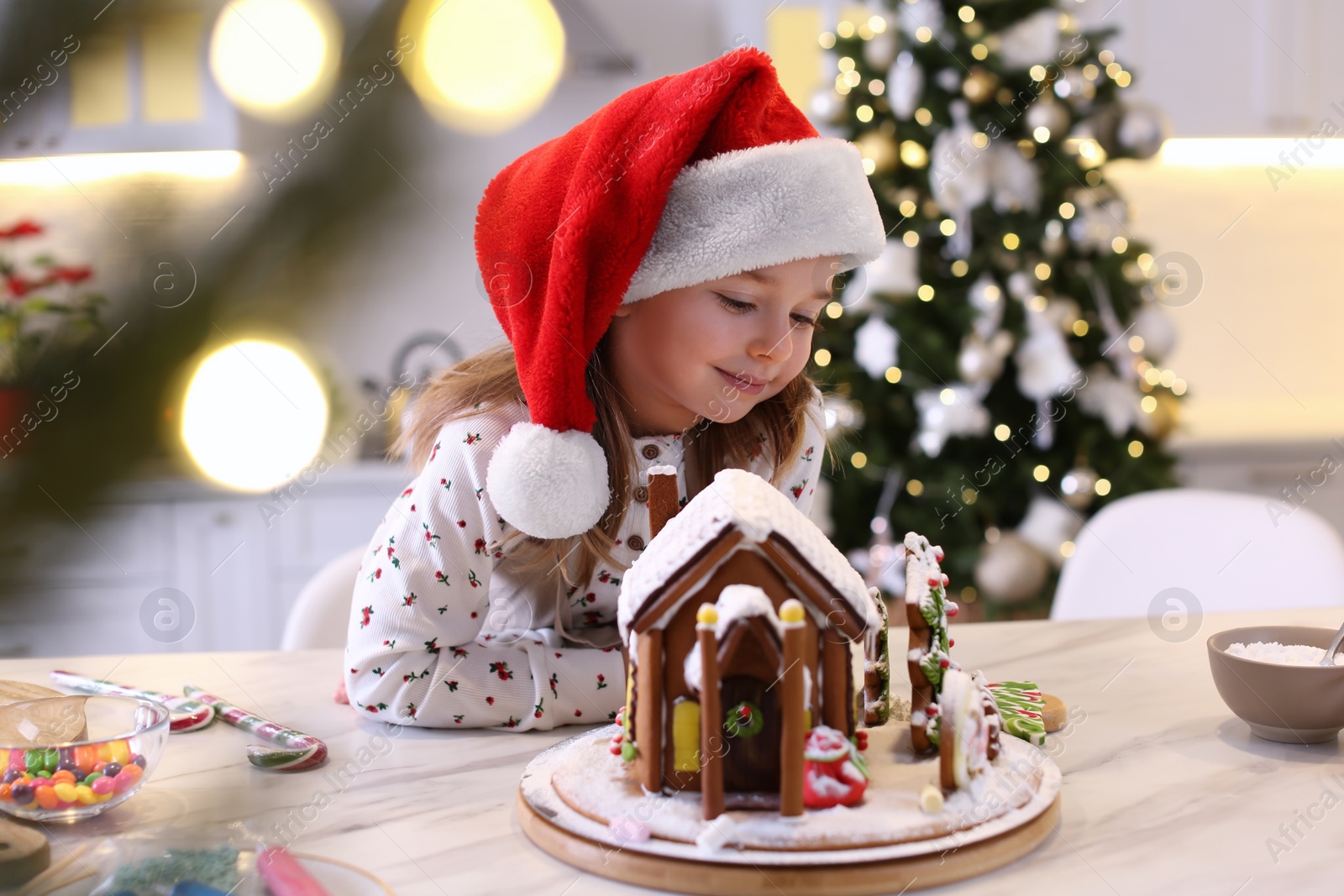 Photo of Cute little girl decorating gingerbread house at table indoors