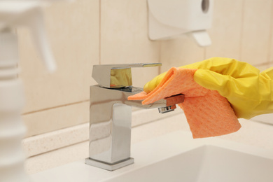 Photo of Person cleaning faucet with rag in bathroom, closeup