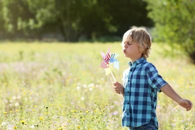 Photo of Cute little boy with pinwheel outdoors, space for text. Child spending time in nature