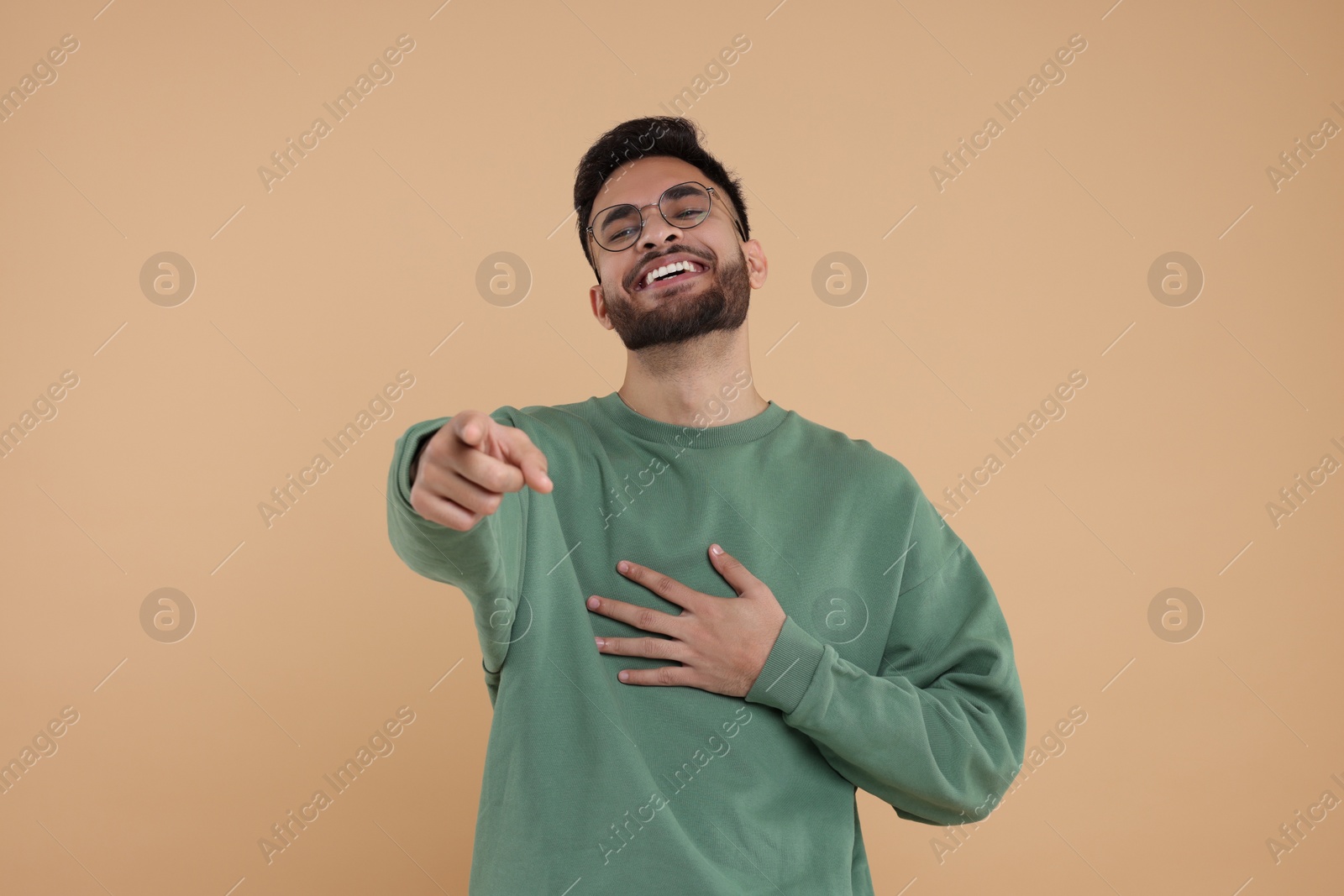 Photo of Handsome young man laughing while pointing at something on beige background