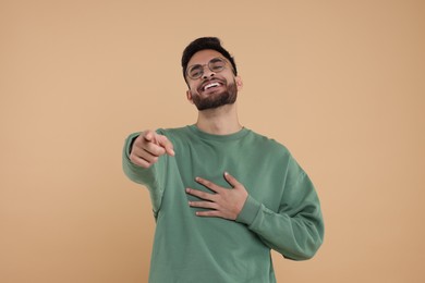 Handsome young man laughing while pointing at something on beige background