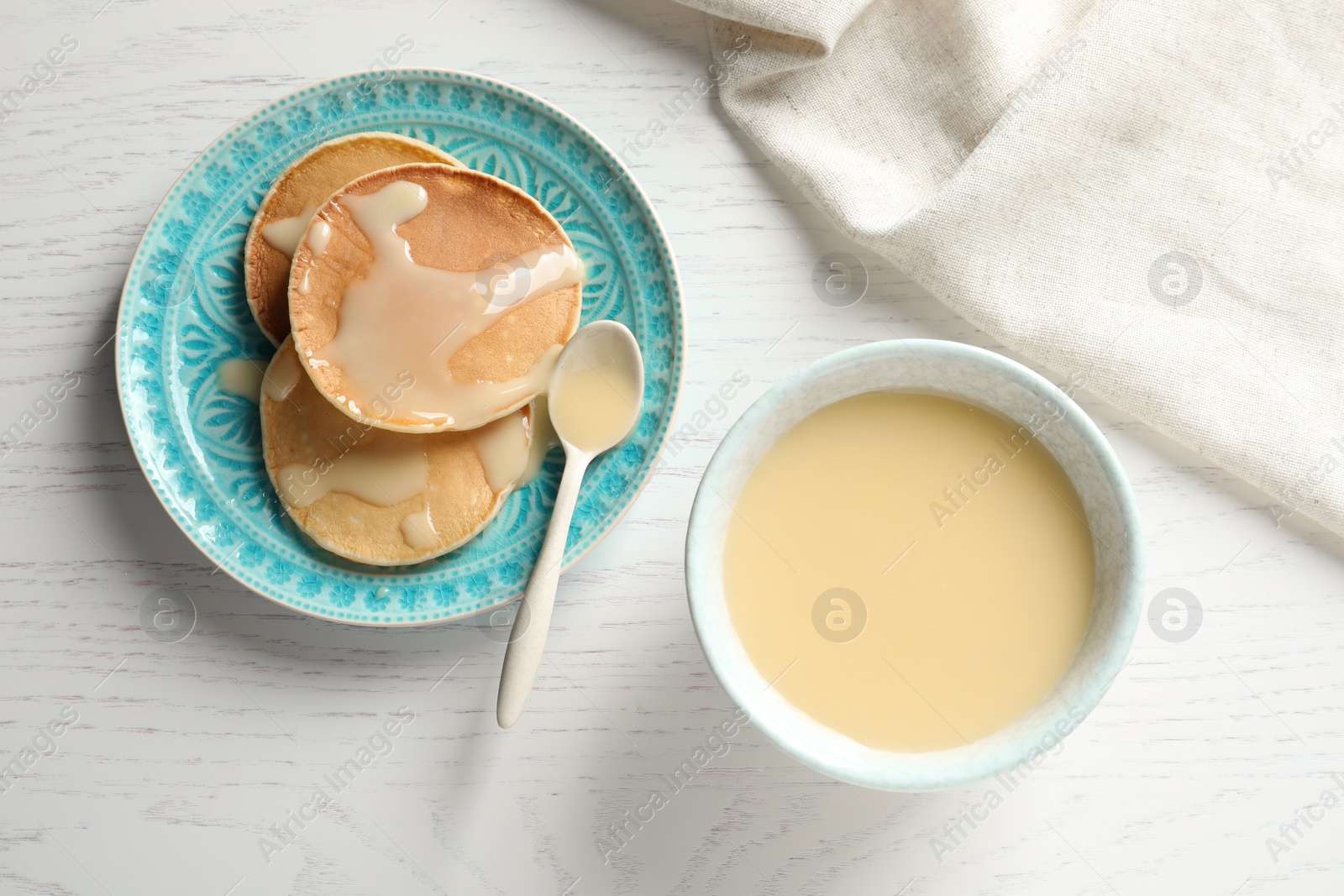 Photo of Bowl of condensed milk and pancakes served on wooden table, top view. Dairy products