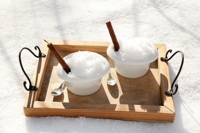 Tray with bowls of tasty ice cream and waffle rolls on snow