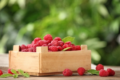 Photo of Wooden crate with delicious ripe raspberries on table against blurred background