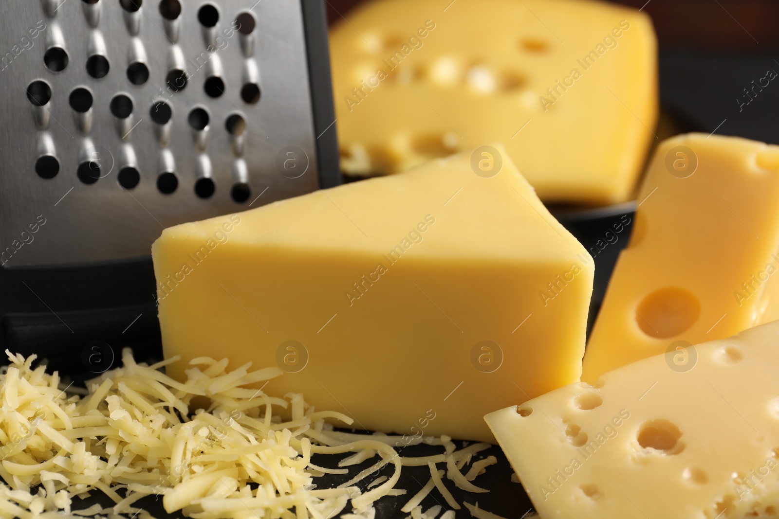 Photo of Grated, cut cheese and grater on black table, closeup