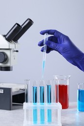 Scientist dripping liquid from pipette into test tube at grey marble table, closeup