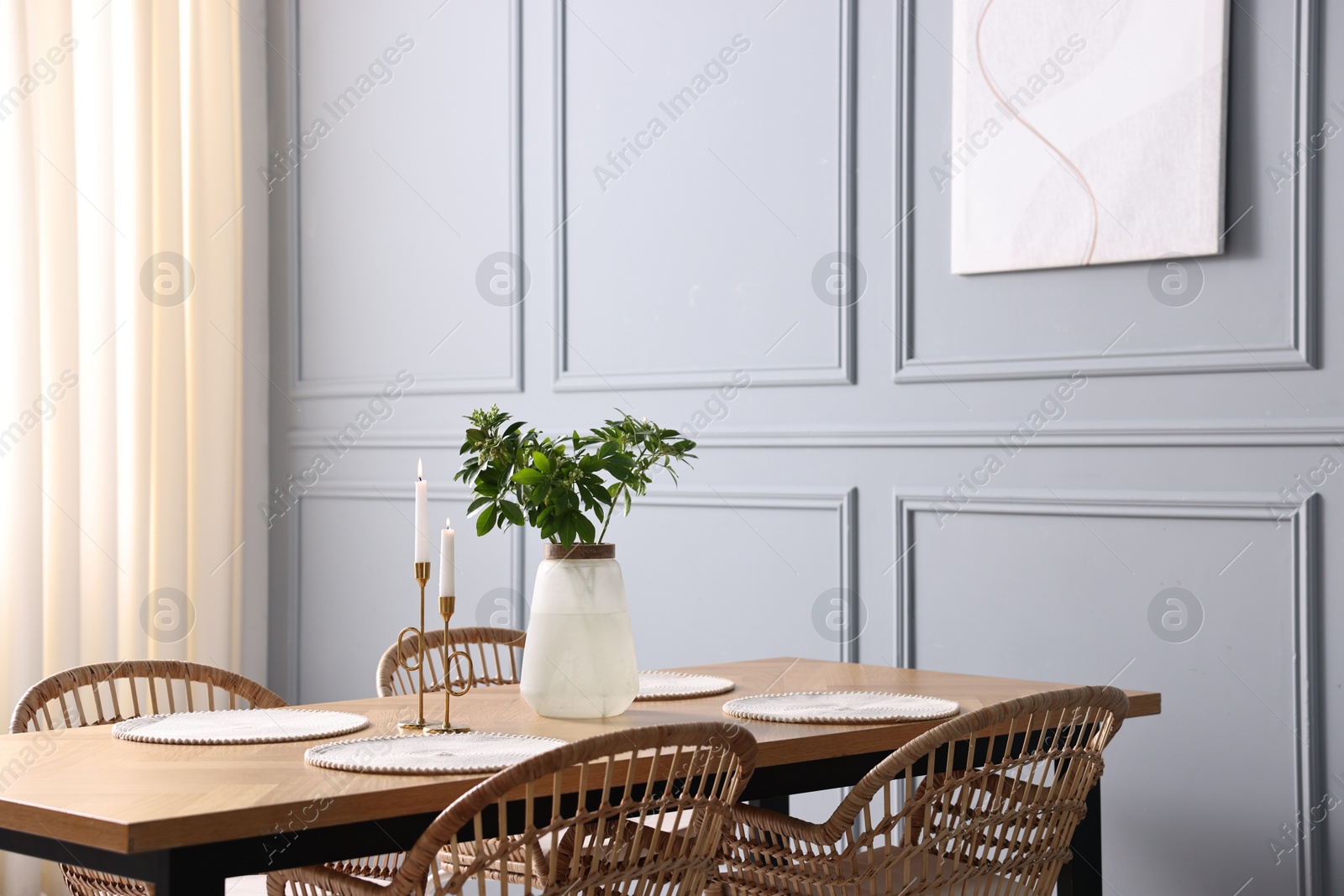 Photo of Rattan chairs, table, burning candles and vase with green branches in stylish dining room