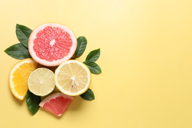 Photo of Different cut citrus fruits and leaves on yellow table, flat lay. Space for text