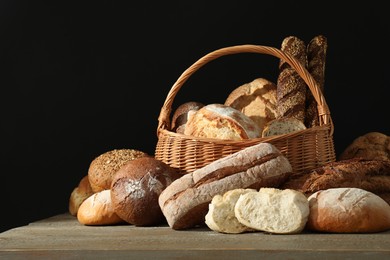 Photo of Wicker basket with different types of fresh bread on wooden table