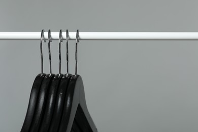 Photo of Black clothes hangers on rack against grey background, closeup. Space for text